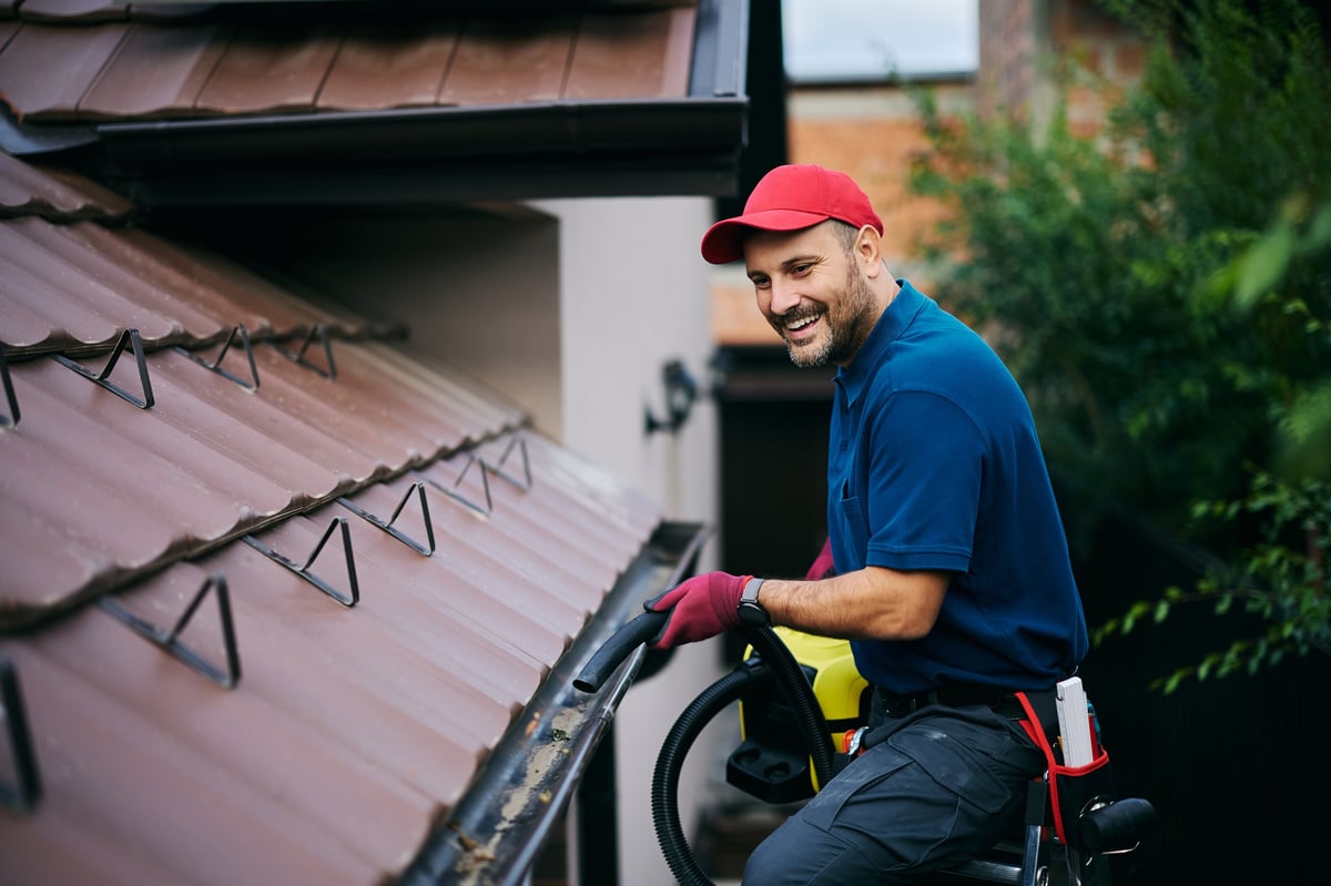 Roofer clearing leaves and moss from a house gutter