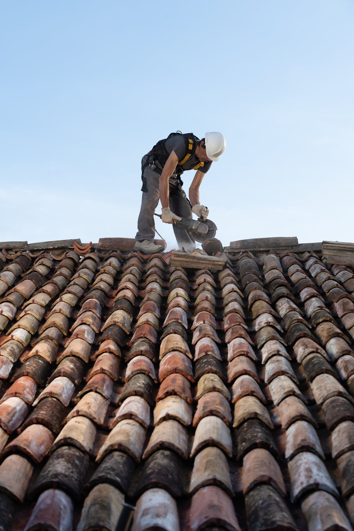 Roofer working on a clay tile roof in a safety harness