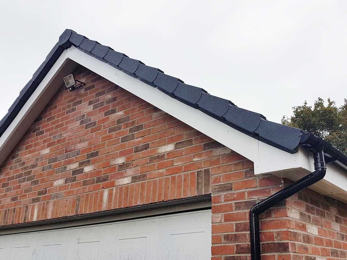 Brick house exterior with white trim, black roof, and downspout near garage entrance — completed guttering and fascia installation