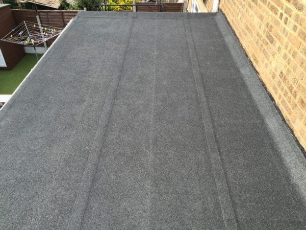 Completed flat rubber roofing on a residential property alongside a brick wall