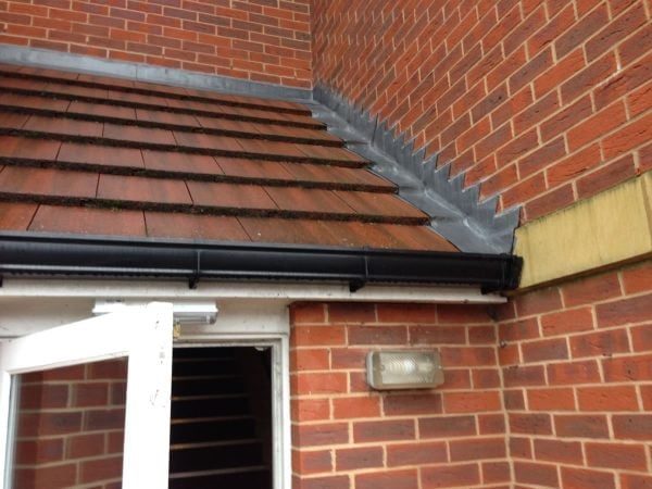 Close-up of brick building exterior showing roof tiles, guttering and lead flashing