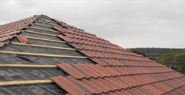 Damaged roof with missing red clay tiles and exposed wood framing — emergency roof repair