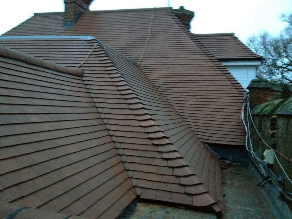 Multi-pitched dark slate roof with multiple angles and chimneys on a traditional British building